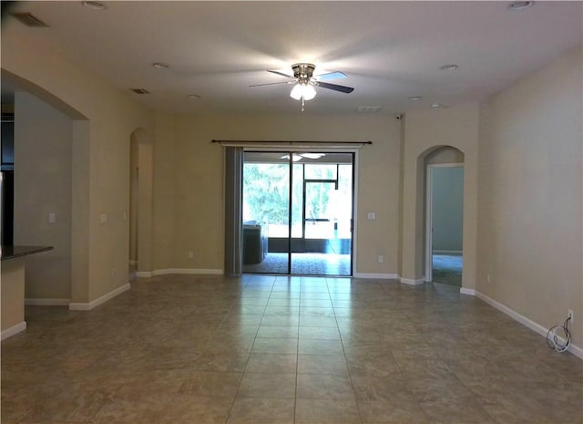 unfurnished room with arched walkways, light tile patterned flooring, visible vents, a ceiling fan, and baseboards