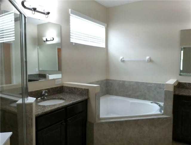 bathroom with a bath, a stall shower, two vanities, and a sink