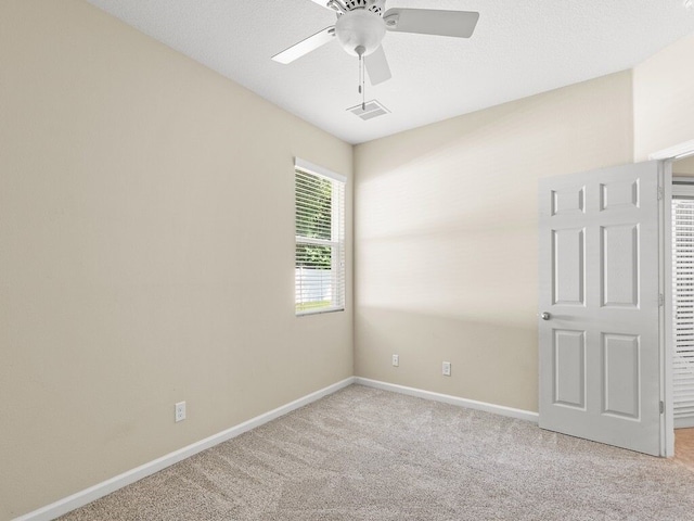 empty room featuring light colored carpet, visible vents, baseboards, and a ceiling fan