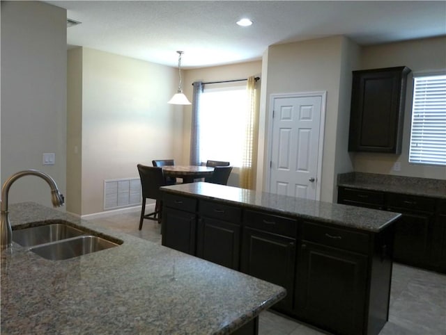 kitchen with visible vents, a center island, dark cabinetry, stone counters, and a sink