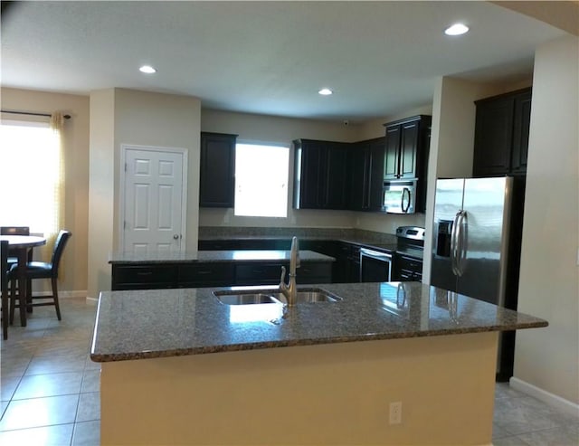 kitchen featuring stainless steel appliances, dark stone counters, a kitchen island with sink, and a sink