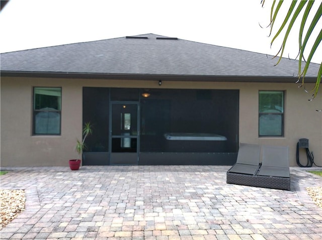 rear view of house with a sunroom, roof with shingles, a patio, and stucco siding