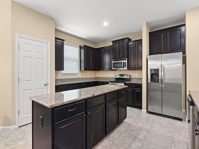 kitchen featuring appliances with stainless steel finishes, dark cabinets, light stone counters, a center island, and light tile patterned floors