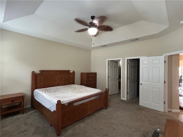 carpeted bedroom with baseboards, visible vents, a raised ceiling, and a ceiling fan