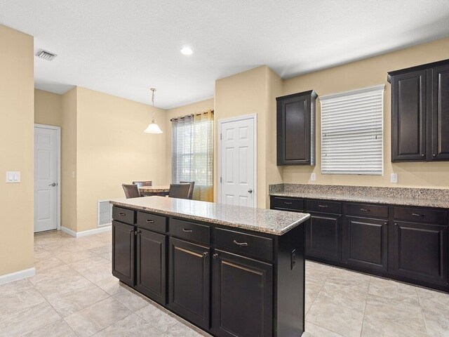 kitchen with hanging light fixtures, dark cabinetry, a center island, and baseboards