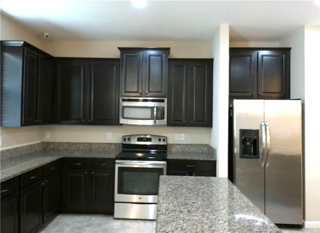 kitchen with light stone countertops, appliances with stainless steel finishes, and dark cabinetry