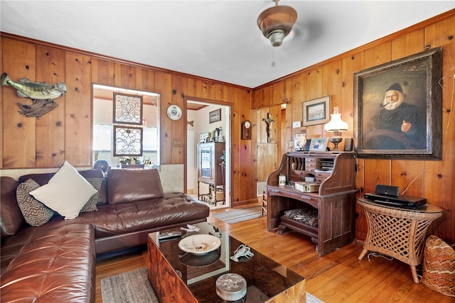 living room with ornamental molding, light hardwood / wood-style floors, wooden walls, and ceiling fan