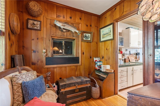 sitting room with ornamental molding, light wood-type flooring, and wooden walls