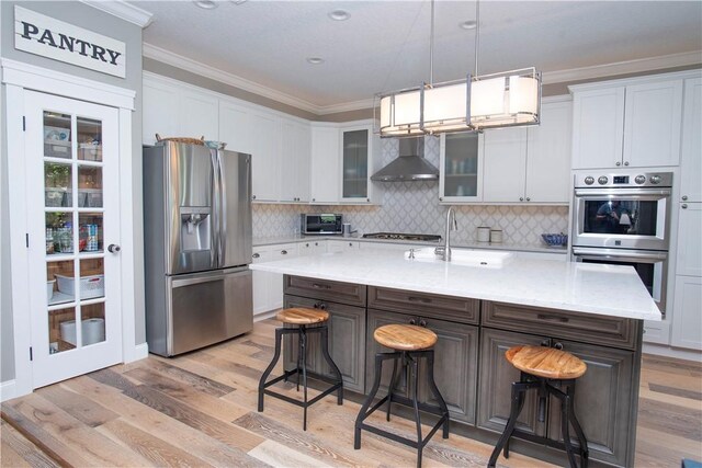 500 45th Ct SW, Vero Beach, FL 32968 - kitchen with appliances with stainless steel finishes, wall chimney exhaust hood, crown molding, a breakfast bar area, and light wood finished floors