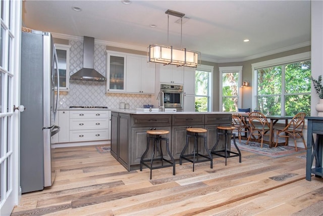 500 45th Ct SW, Vero Beach, FL 32968 - kitchen with wall chimney exhaust hood, stainless steel appliances, ornamental molding, white cabinets, and light wood finished floors