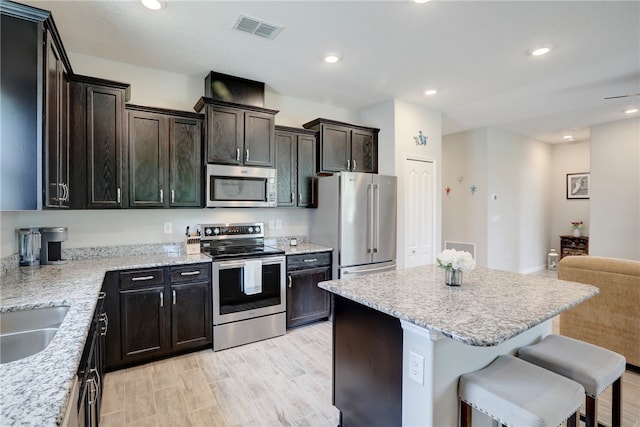 kitchen featuring light stone counters, stainless steel appliances, light hardwood / wood-style floors, a breakfast bar area, and a center island