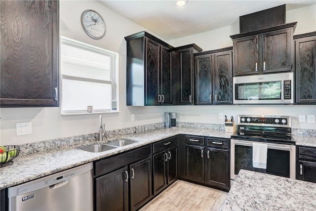 kitchen with dark brown cabinetry, sink, light stone counters, and appliances with stainless steel finishes