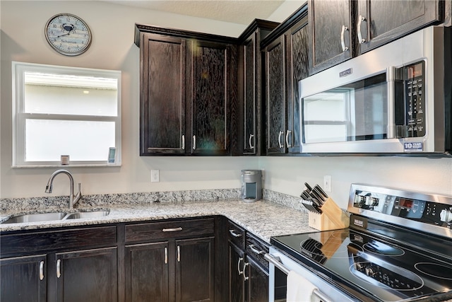 kitchen featuring light stone countertops, dark brown cabinets, sink, and appliances with stainless steel finishes