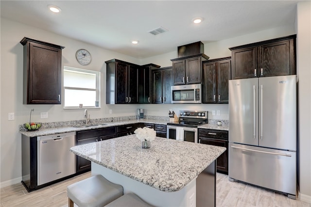 kitchen featuring light stone counters, a center island, sink, a kitchen breakfast bar, and appliances with stainless steel finishes