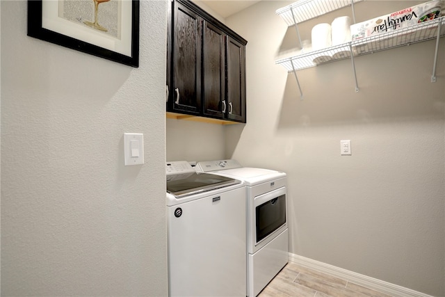 washroom featuring cabinets, washing machine and dryer, and light hardwood / wood-style flooring