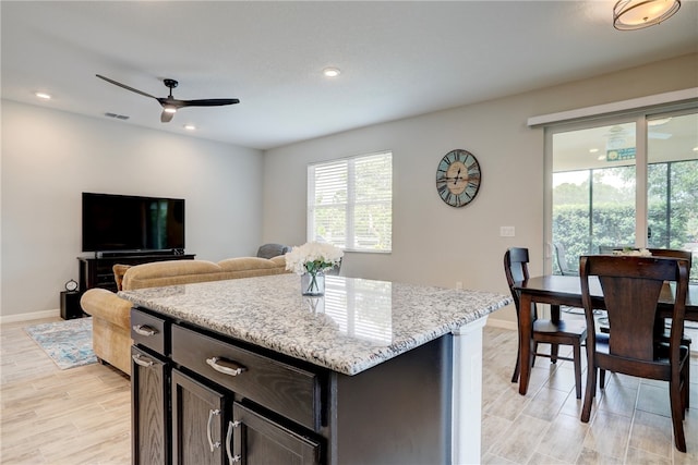 kitchen with ceiling fan, light wood-type flooring, light stone counters, and a center island