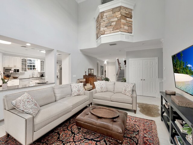 tiled living room featuring a towering ceiling, sink, and crown molding