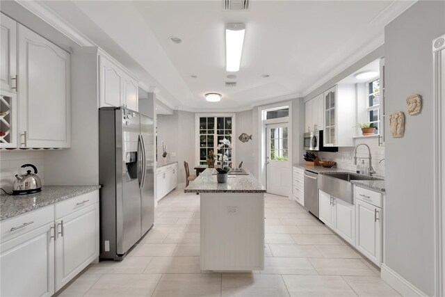 kitchen with white cabinets, appliances with stainless steel finishes, light stone counters, and a center island