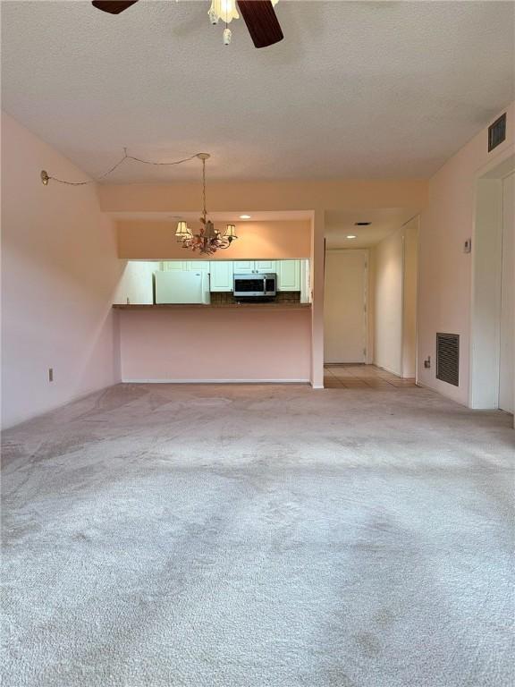 unfurnished living room with visible vents, a textured ceiling, and ceiling fan with notable chandelier