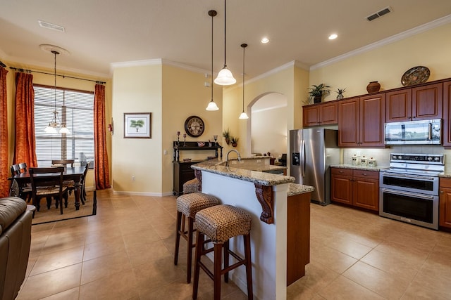 kitchen with a center island with sink, a kitchen breakfast bar, crown molding, light stone countertops, and appliances with stainless steel finishes