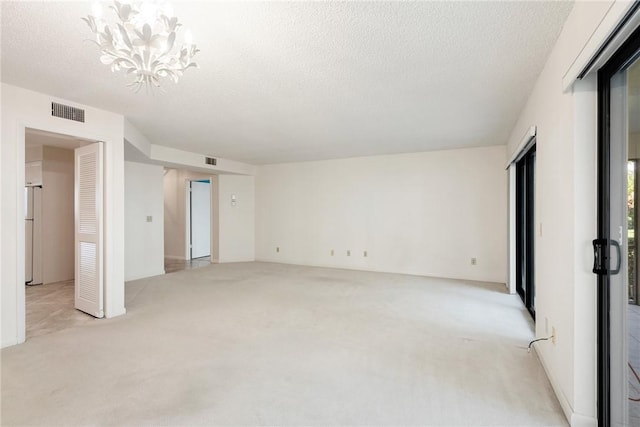 carpeted spare room with a textured ceiling and a notable chandelier