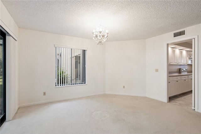 empty room featuring light colored carpet, a textured ceiling, and a chandelier