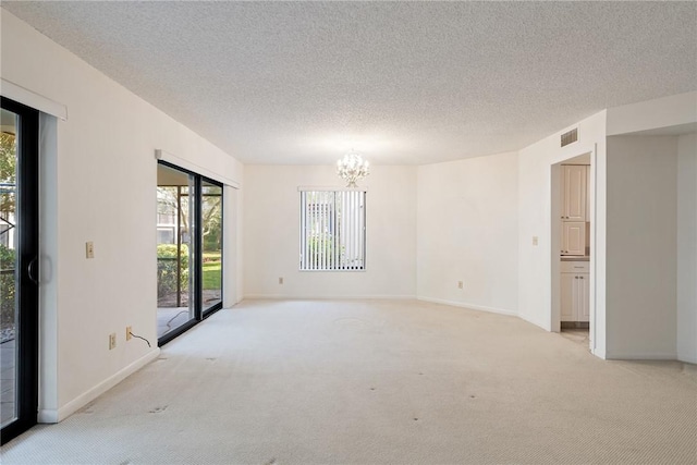 unfurnished room featuring a textured ceiling, light carpet, and an inviting chandelier