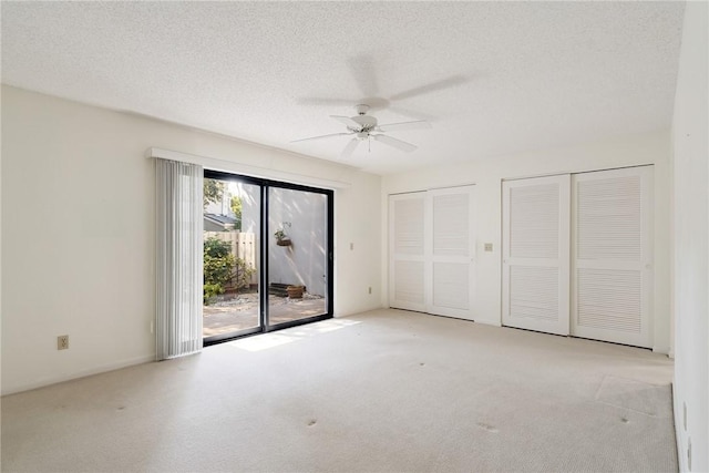 unfurnished bedroom with ceiling fan, multiple closets, access to exterior, light colored carpet, and a textured ceiling