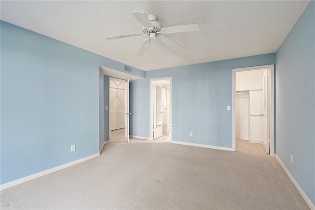 unfurnished bedroom featuring ceiling fan, a walk in closet, a closet, and light colored carpet