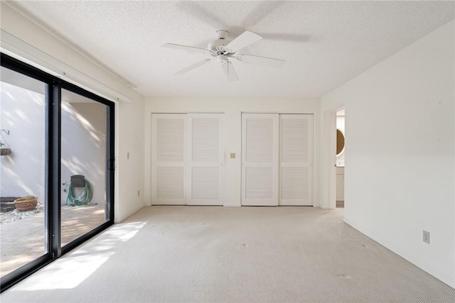 unfurnished bedroom featuring ceiling fan, access to exterior, a textured ceiling, and two closets