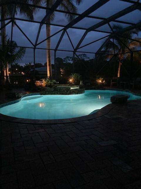 view of swimming pool featuring glass enclosure, a pool with connected hot tub, and a patio