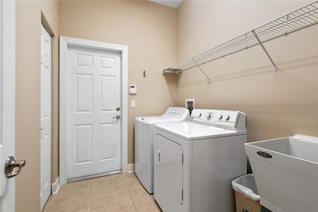 clothes washing area with washer and dryer, laundry area, light tile patterned flooring, and a sink