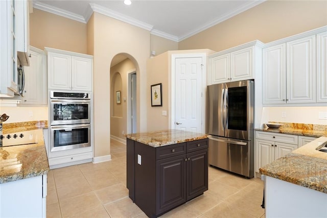 kitchen with light stone countertops, arched walkways, ornamental molding, appliances with stainless steel finishes, and white cabinetry