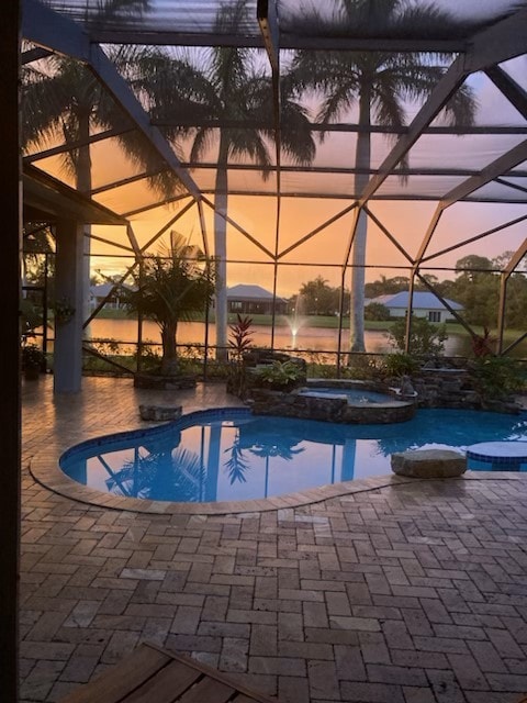 pool at dusk with glass enclosure, a patio, and a pool with connected hot tub