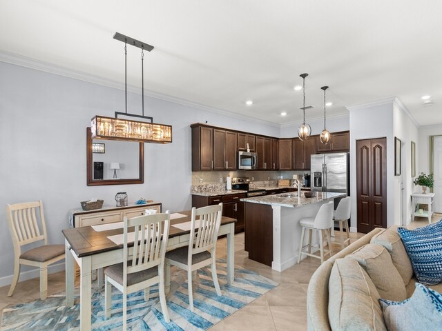 kitchen featuring light tile patterned flooring, appliances with stainless steel finishes, a breakfast bar area, hanging light fixtures, and a kitchen island with sink