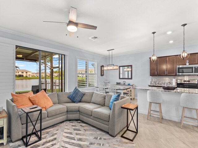 living room with a water view, ceiling fan, crown molding, and light tile patterned floors