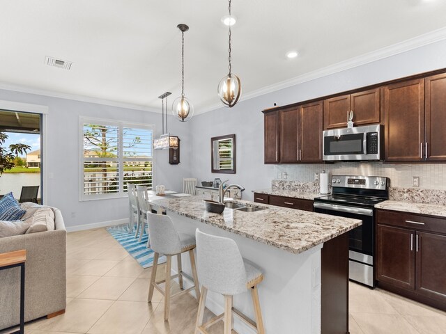 kitchen with backsplash, appliances with stainless steel finishes, hanging light fixtures, sink, and a kitchen island with sink