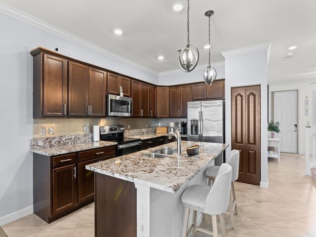 kitchen featuring stainless steel appliances, sink, light stone counters, hanging light fixtures, and a kitchen island with sink