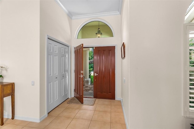 entryway with crown molding, baseboards, light tile patterned floors, and a high ceiling