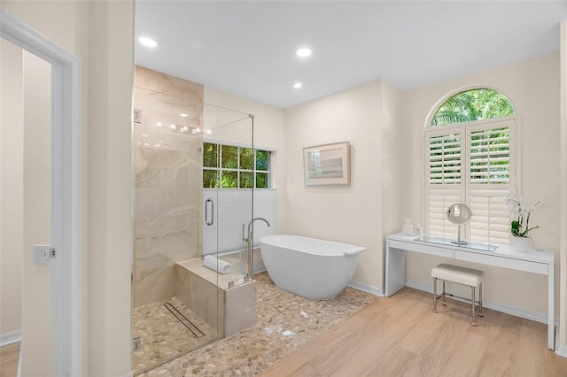 full bathroom with a freestanding bath, wood finished floors, and a healthy amount of sunlight