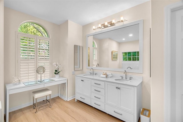full bath with double vanity, a sink, baseboards, and wood finished floors