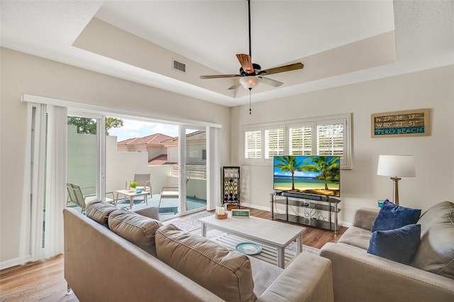 living room featuring light wood-type flooring, ceiling fan, and a raised ceiling