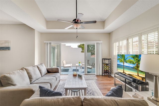 living room featuring light wood-type flooring, ceiling fan, and a raised ceiling