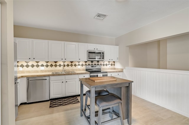 kitchen with stainless steel appliances, white cabinetry, sink, a kitchen bar, and decorative backsplash