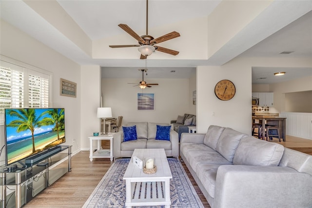 living room with light hardwood / wood-style floors, ceiling fan, and a tray ceiling