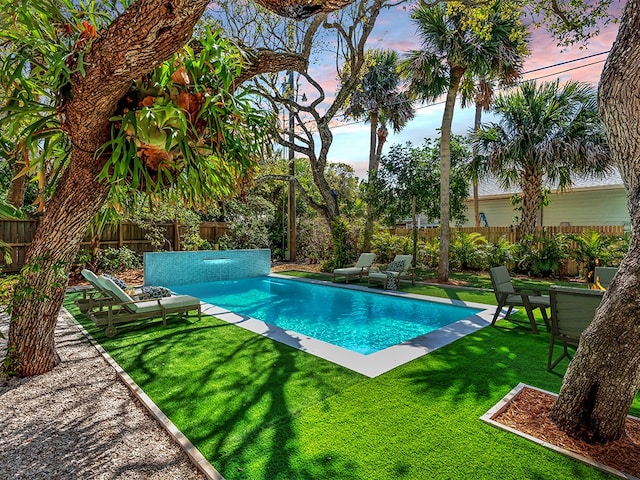 pool at dusk featuring a yard