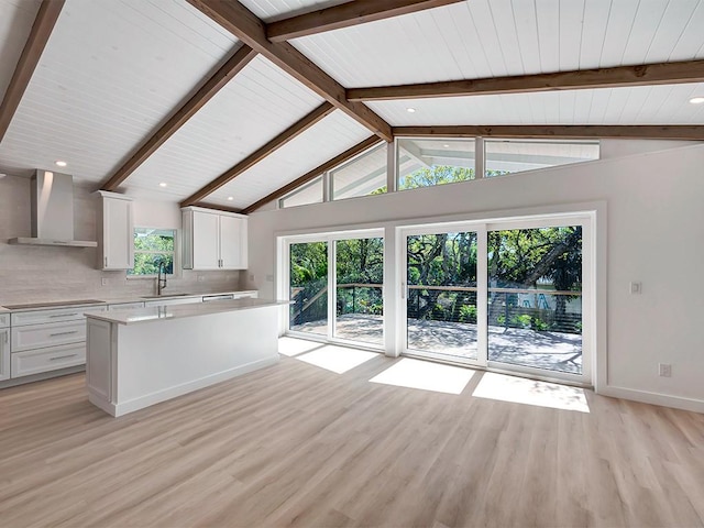 kitchen with vaulted ceiling with beams, white cabinetry, and wall chimney exhaust hood