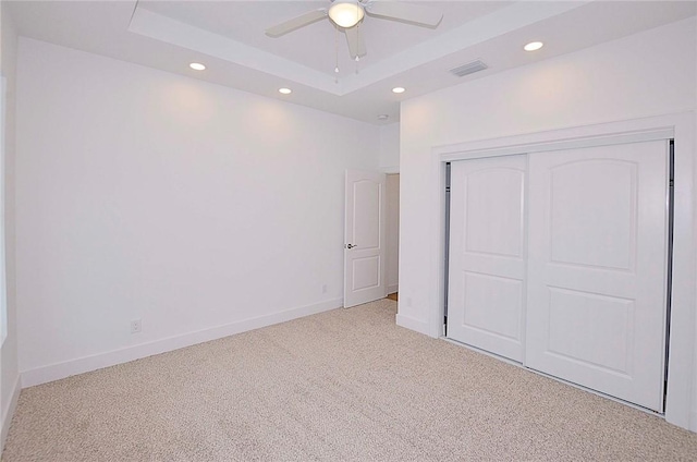 unfurnished bedroom with a raised ceiling, a closet, ceiling fan, and light colored carpet