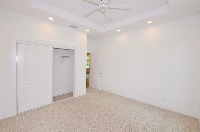 unfurnished bedroom featuring ceiling fan, light colored carpet, a closet, and a raised ceiling