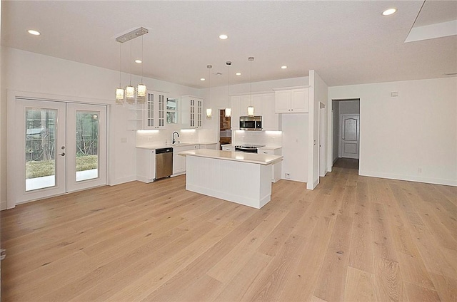 kitchen with stainless steel appliances, decorative light fixtures, a center island, white cabinetry, and french doors